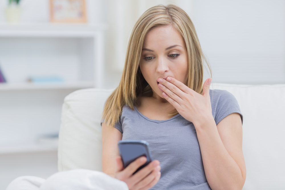 Young woman looking at a text message on her phone in surprise