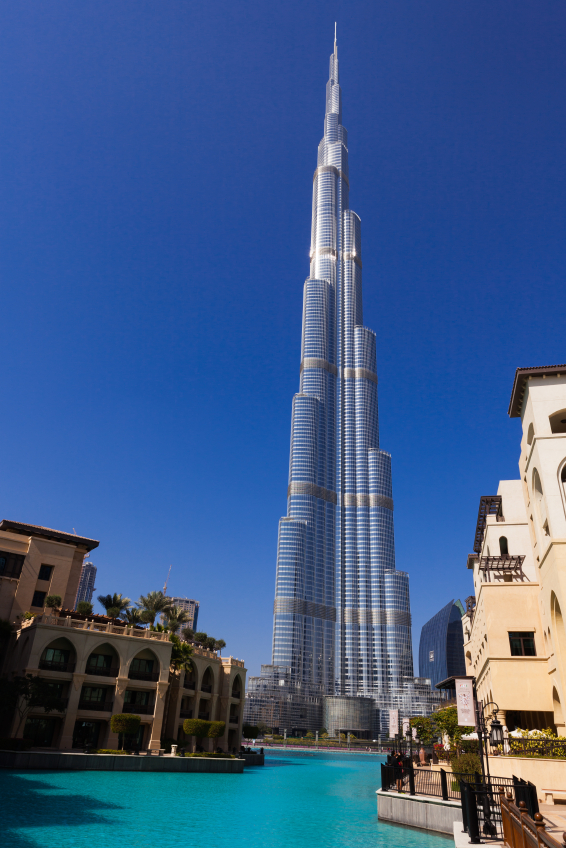 Dubai, United Arab Emirates - January 27, 2012:  The Burj Khalifa, the tallest building in the world, stands tall above all the buildings in Dubai, United Arab Emirates.  The Armani Hotel occupies several floors of the tower and on the first few floors is Dubai Mall.  Photo shot in the afternoon sunlight against a rare clear blue, cloudless sky with white clouds.  The sun reflects off the top of the building.