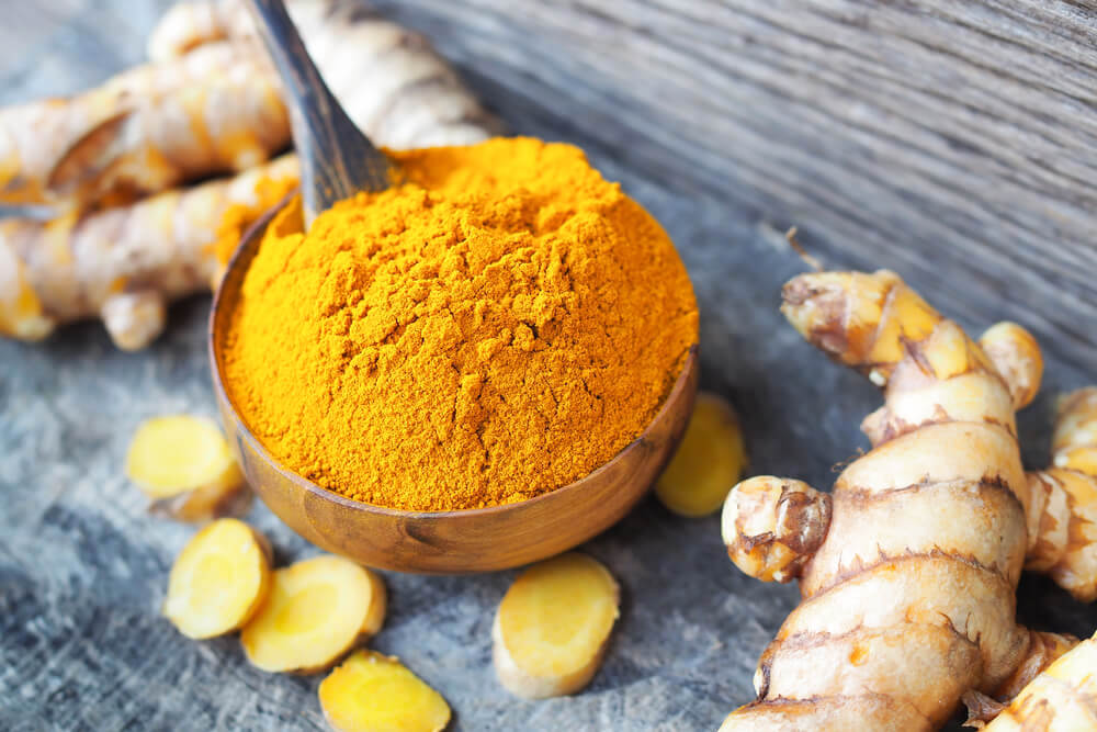Turmeric powder in a small scoop, surrounded by fresh turmeric root 