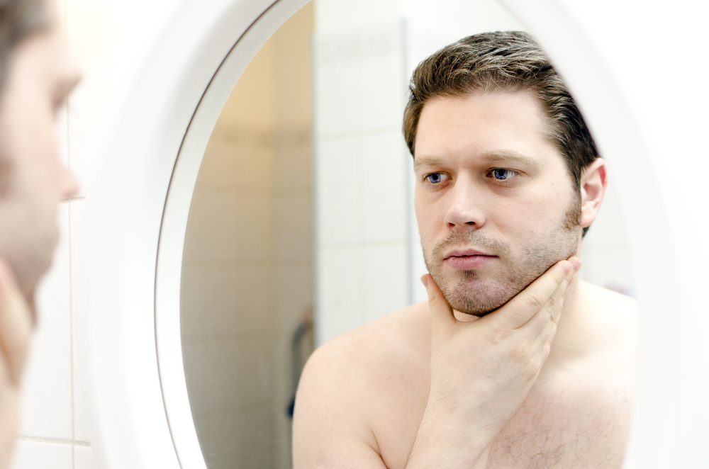 Man looking at his skin in the mirror. 