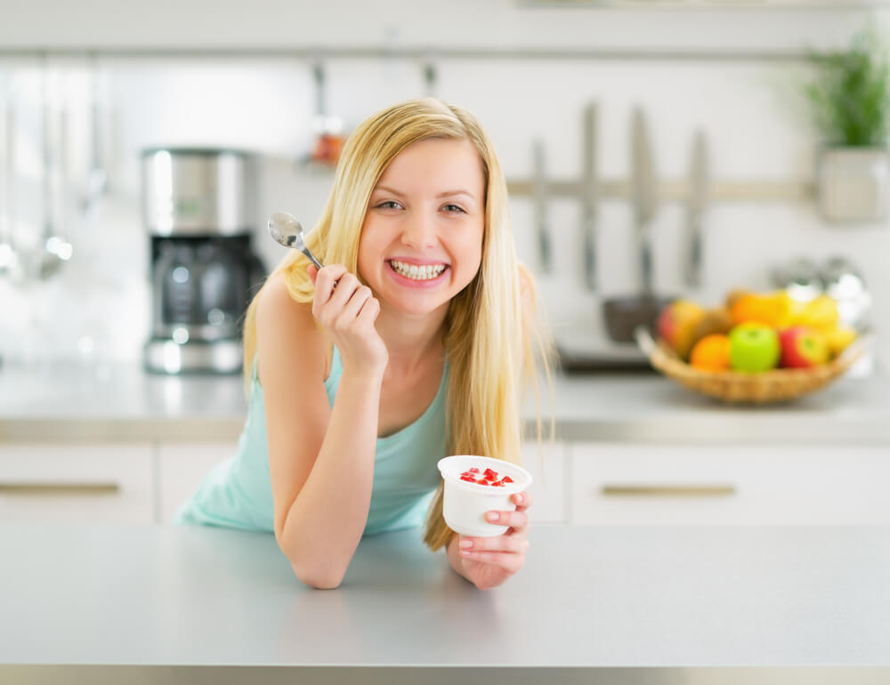 Smiling woman eating yogurt in kitchen