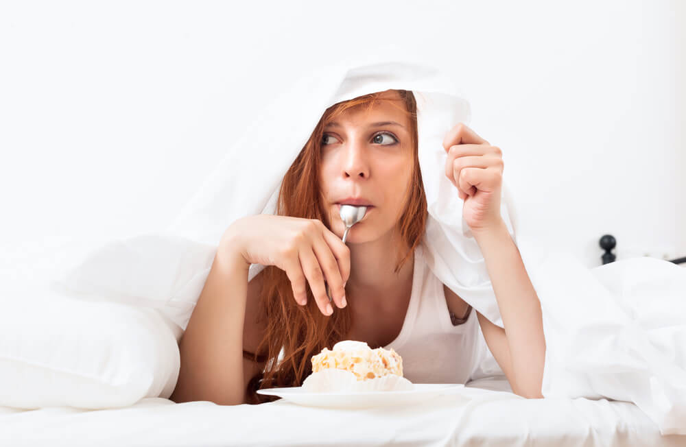 woman eating ice cream under bed sheets