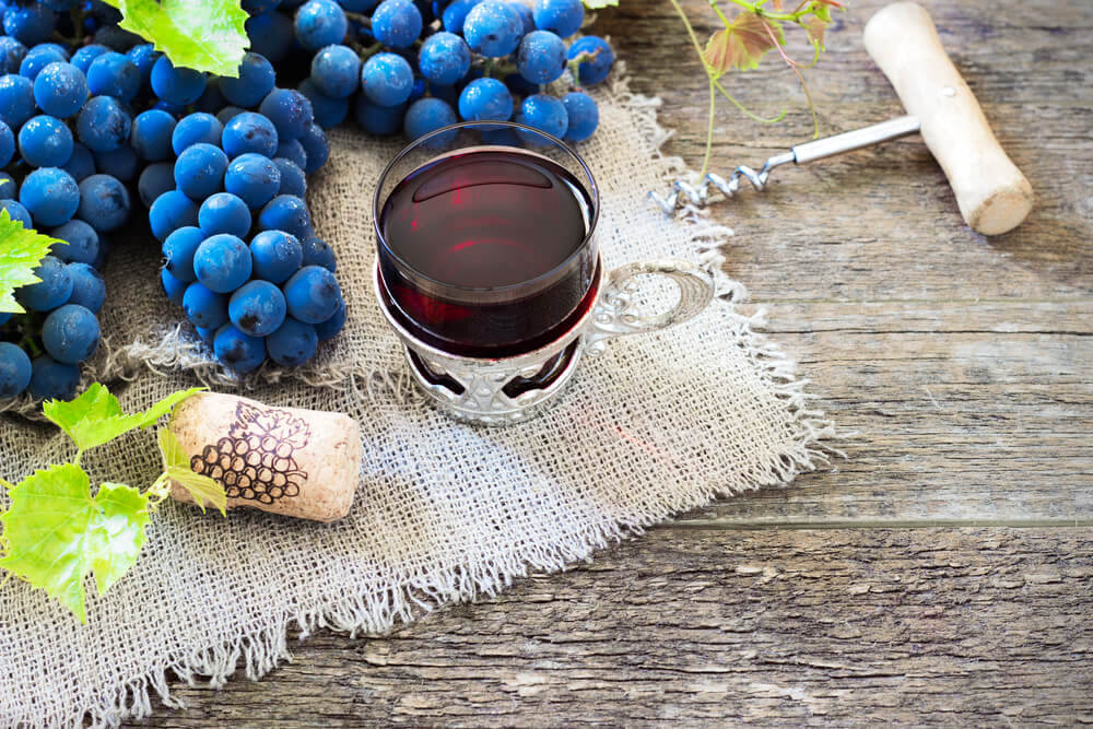 Small glass of red wine surrounded by grapes