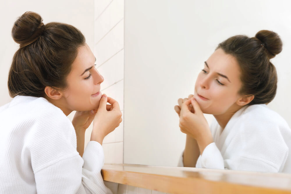 Woman popping pimple in the bathroom mirror