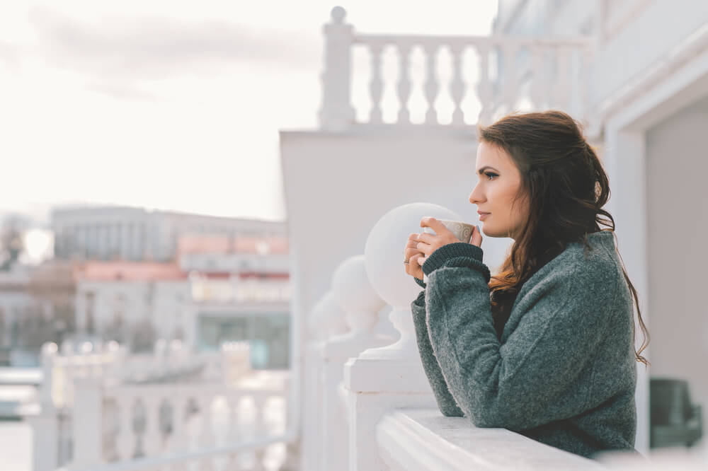 Young woman in long jumper drinking hot tea on a cold winter's day, on the balcony