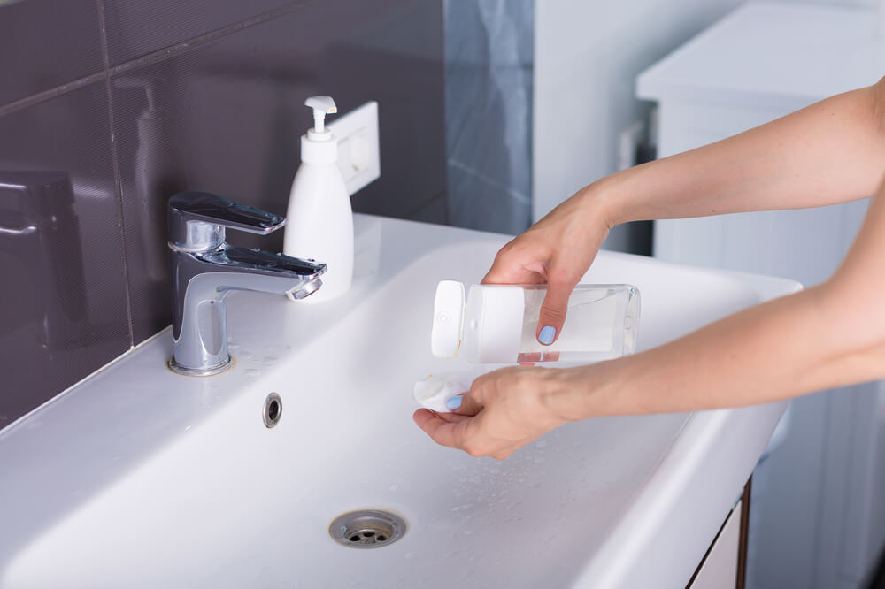 Woman pouring out micellar water in a cotton pad over the sink 
